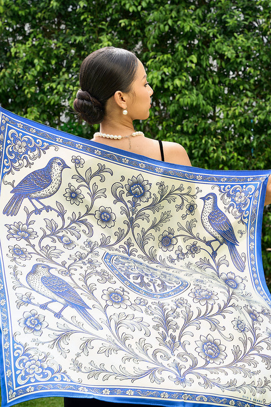 Blue and ivory chinoiserie bird print twill silk scarf held open behind the shoulders, garden background