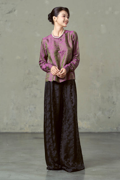 Model in magenta olive floral silk jacquard blouse and pearls with black wide-leg trousers, full length