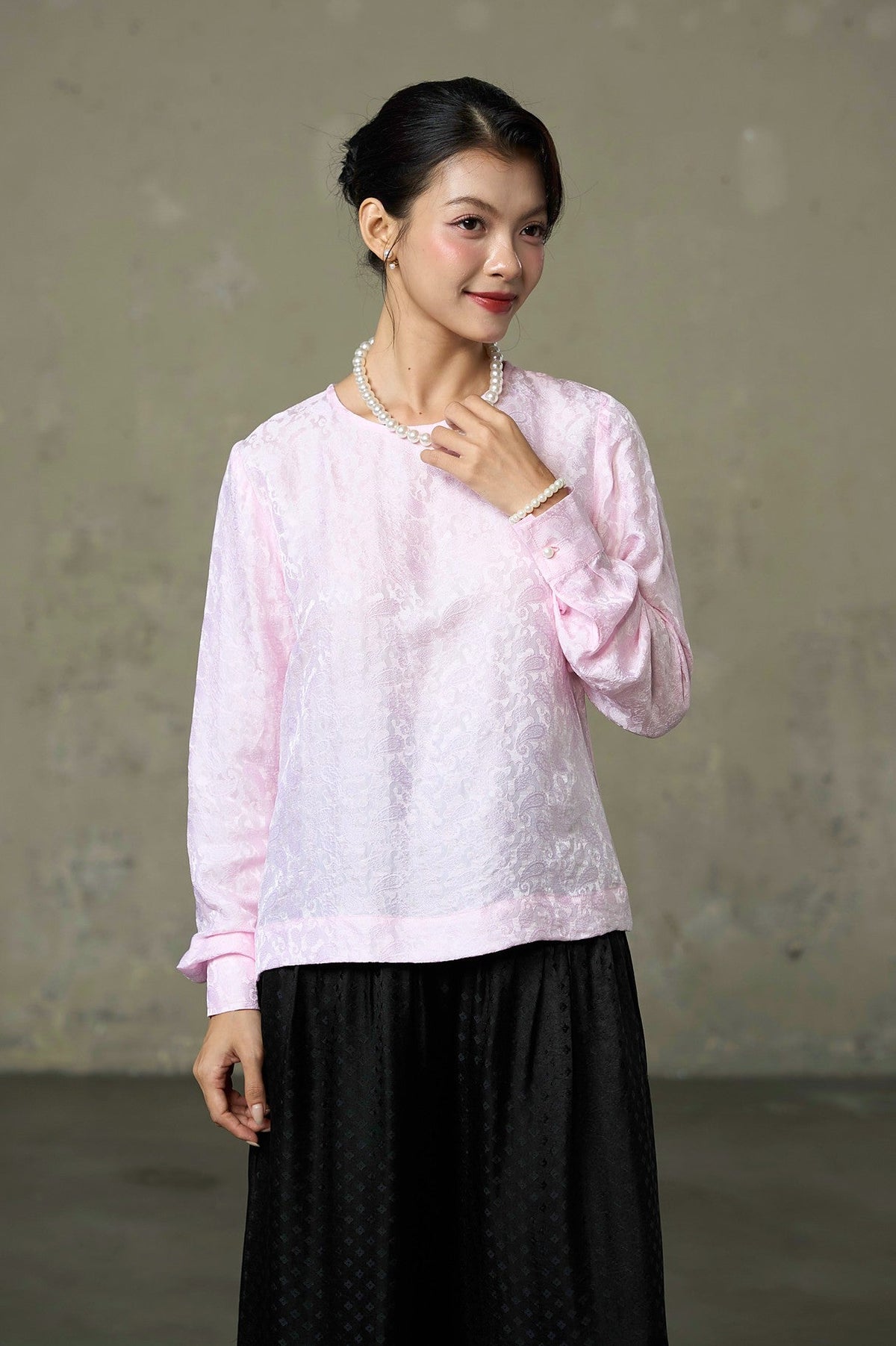 Pink silk jacquard blouse with round neck and buttoned cuffs, worn with black wide-leg trousers