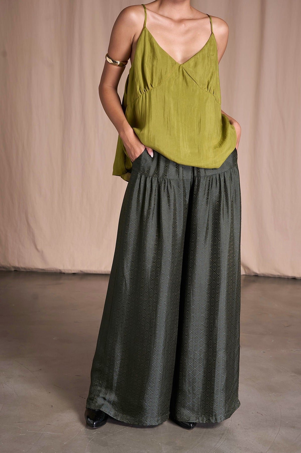 Model in Portia Khaki Diamond silk wide-leg trousers with hands in the side pockets and an olive silk camisole