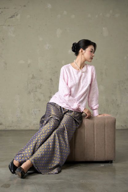 Model seated in Portia Dusk Gold blue-violet and gold silk jacquard wide-leg trousers with a pink silk blouse