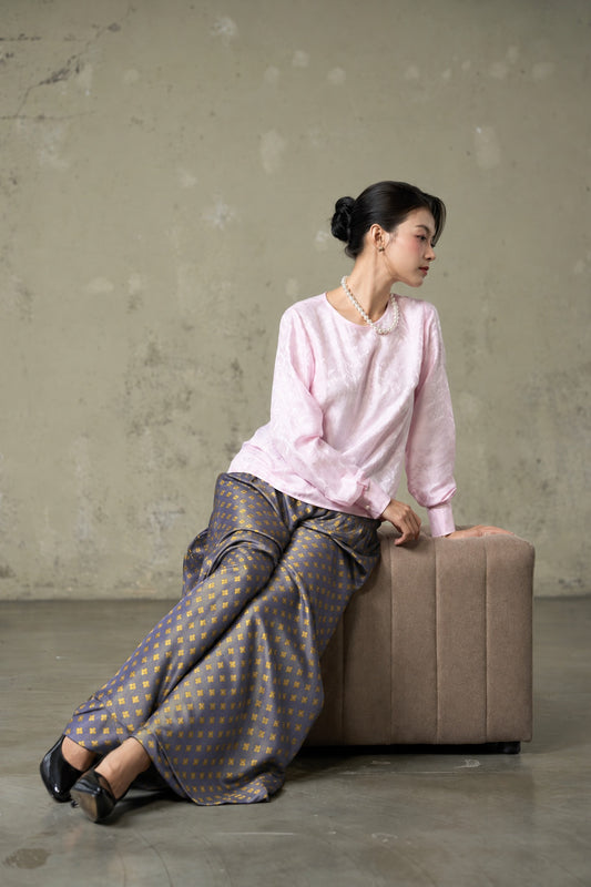 Model seated in Portia Dusk Gold blue-violet and gold silk jacquard wide-leg trousers with a pink silk blouse