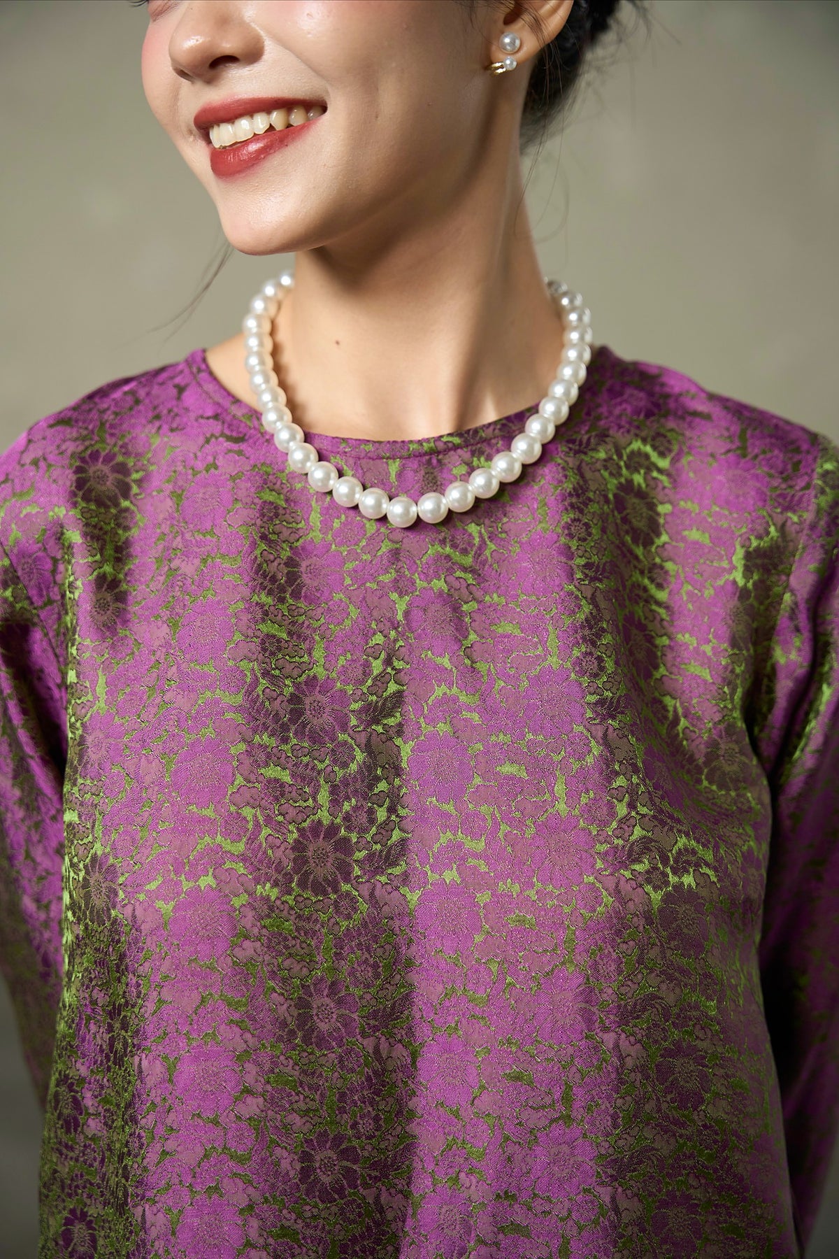 Close-up of the magenta and olive shot silk jacquard at the round neckline, worn with pearls