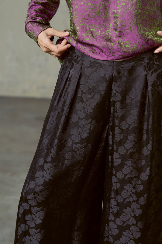 Close-up of black silk jacquard trousers showing hip pleats and large woven peony