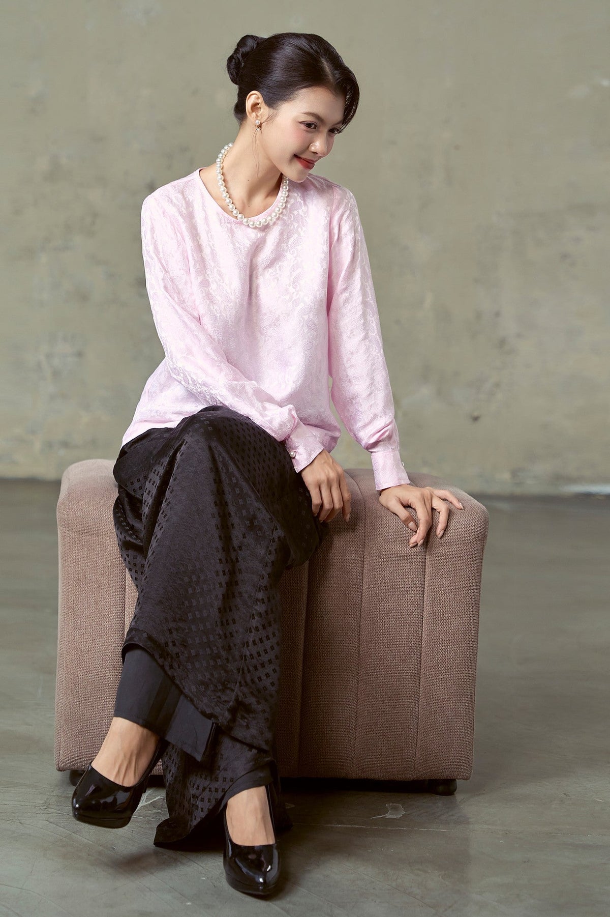 Model seated in blush pink silk jacquard blouse and black jacquard wide-leg trousers