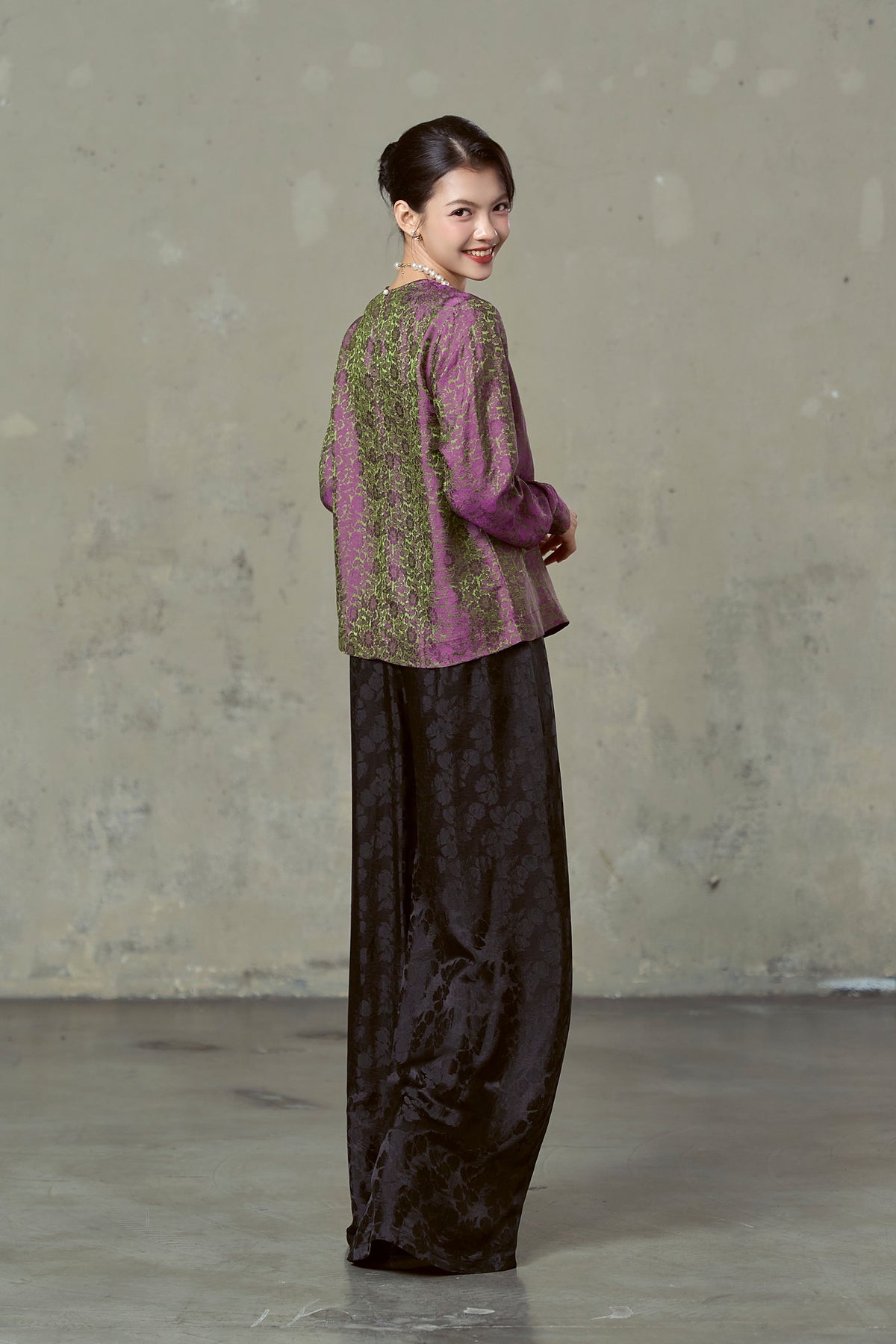 Model turning to look back in magenta and olive silk jacquard blouse, showing the shot colour