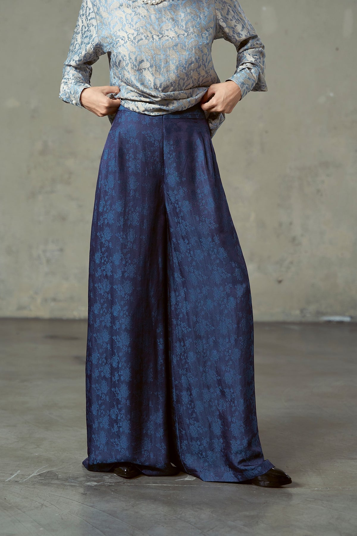 Close-up of navy silk jacquard trousers showing hip pleats and blue woven floral
