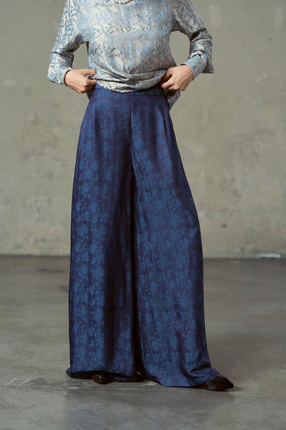 Close-up of navy silk jacquard trousers showing hip pleats and blue woven floral