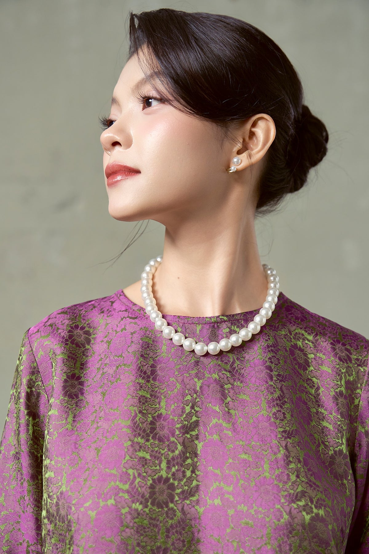 Three-quarter close-up of magenta silk jacquard blouse with olive floral and pearl necklace