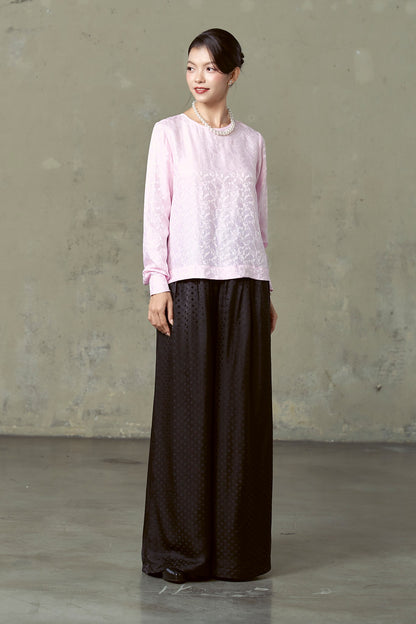 Three-quarter view of black silk jacquard wide-leg trousers worn with pink blouse